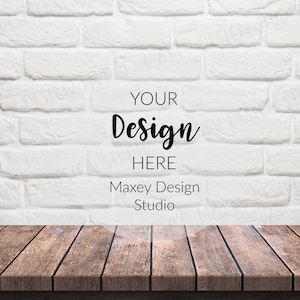 以下が含まれることがあります： 白いレンガの壁の背景に、手前に木製のテーブルがあります。壁に「YOUR Design HERE Maxey Design Studio」というテキストが重ねられています。