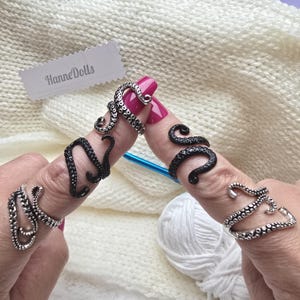 Op de afbeelding: Drie ringen in de vorm van inktvistentakels, met twee zilverkleurige ringen en één zwarte ring. Elke ring heeft een textuur met kleine ronde zuignapdetails. De ringen worden om de vingers gedragen, met een wit label met de tekst HanneDolls.