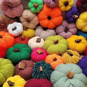 May include: A selection of knitted pumpkins in a variety of colours, such as orange, green, yellow, and purple. Each pumpkin has a brown stem. These decorative pumpkins are ideal for autumn and fall decorations.