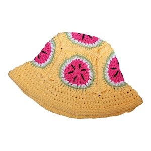 Op de afbeelding: Een gehaakte bucket hat van lichtgeel garen met meerdere cirkelvormige motieven die lijken op watermeloenpartjes. Elk motief heeft een felroze centrum, een witte rand en een lichtgroene buitenring met zwarte geborduurde zaadjes.