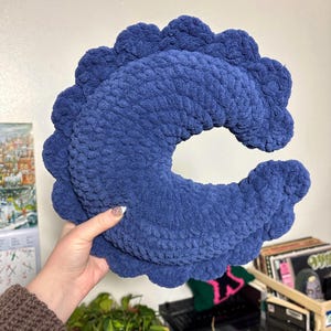 Könnte beinhalten: Ein blaues, gehäkeltes Kissen in Halbmondform mit einem gewellten Rand.