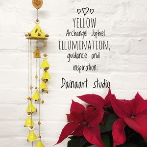 Peut inclure: Carillon en céramique jaune avec un motif de maison et de croissant de lune. Le carillon est suspendu à un mur de briques blanches avec une plante de poinsettia rouge dans le coin. Le texte "YELLOW ArchAngel Jophiel ILLUMINATION, guidance and inspiration. Dainaaart studio" est écrit sous le carillon.