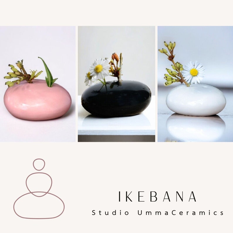 May include: Three small, round ceramic vases in pink, black, and white, each with a single flower arrangement. The vases are shaped like pebbles and are arranged in a row. The text "IKEBANA Studio UmmaCeramics" is below the vases.