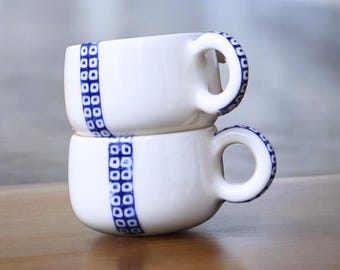 Może przedstawiać: Dwa białe ceramiczne kubki do kawy z niebieskimi i białymi geometrycznymi wzorami ułożone jeden na drugim.
