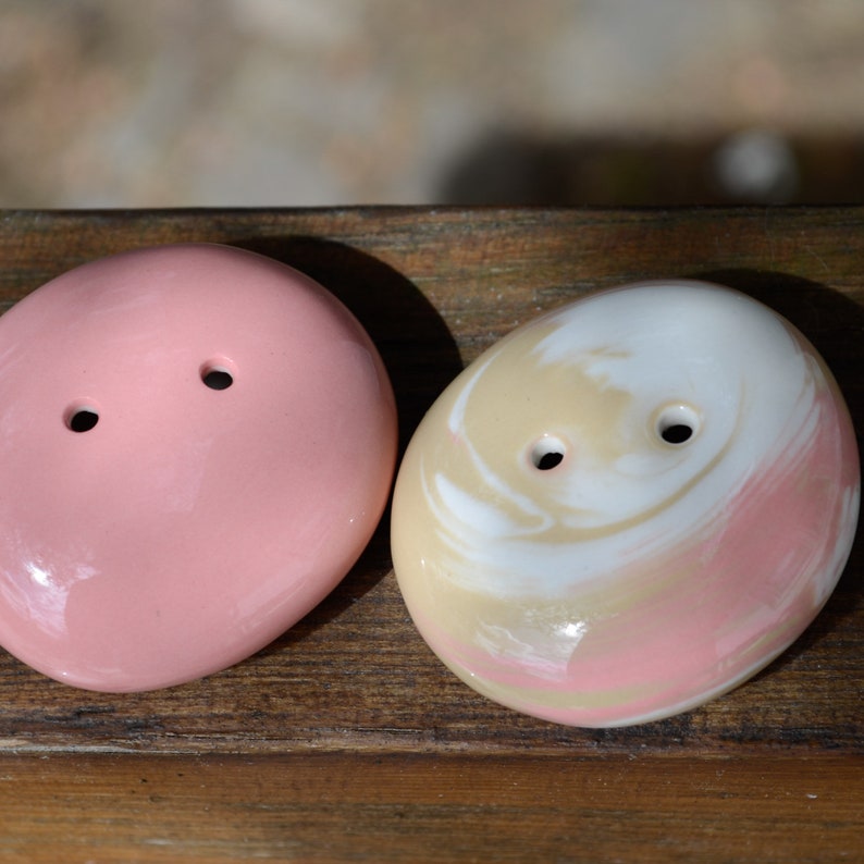 May include: Two ceramic buttons, one pink and one with a swirl pattern of white, pink, and beige.
