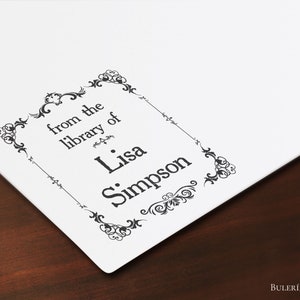 Puede incluir: Un sello en blanco y negro con un borde decorativo. El sello dice "from the library of Lisa Simpson".