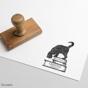 K&ouml;nnte beinhalten: Ein schwarzer und wei&szlig;er Stempel mit einer Silhouette einer Katze, die auf drei B&uuml;chern sitzt. Der Text "Ex libris" und "Cristine Pastranza" ist auf den B&uuml;chern gedruckt.