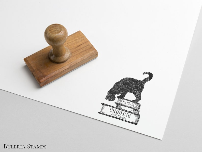 K&ouml;nnte beinhalten: Ein schwarzer und wei&szlig;er Stempel mit einer Silhouette einer Katze, die auf drei B&uuml;chern sitzt. Der Text "Ex libris" und "Cristine Pastranza" ist auf den B&uuml;chern gedruckt.