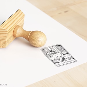 May include: A wooden stamp with a handle and a rectangular base. The stamp features a black and white illustration of a person reading in a library with the text "La libra" and "Michael Smith".