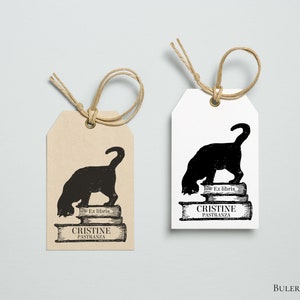 K&ouml;nnte beinhalten: Zwei braune und wei&szlig;e Geschenkanh&auml;nger mit einer schwarzen Silhouette einer Katze, die einen Stapel B&uuml;cher liest. Der Text auf den Anh&auml;ngern lautet "Ex libris Cristine Pastranza".