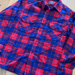 Peut inclure: Une chemise en flanelle à carreaux rouge, bleu et blanc avec un devant boutonné et des manches longues. La chemise a deux poches poitrine et une étiquette "Wrangler" sur le col.