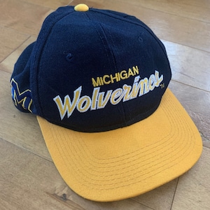 May include: A navy blue and yellow baseball cap with the text "MICHIGAN WOLVERINES" embroidered on the front.