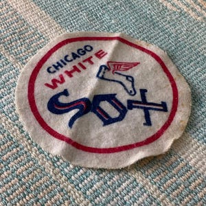 May include: A circular, off-white patch with a red border. The text "CHICAGO WHITE" is arched across the top in red, with "SOX" in blue below. A winged horse graphic is above the "SOX".