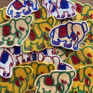 May include: A selection of colourful felt elephant appliques. The elephants are in various colours, including yellow, cream, and white, with red, blue, and green embroidered details. The appliques are scattered across the image.