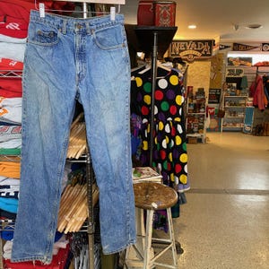 May include: Light blue denim jeans hanging on a metal rack. The jeans have a classic five-pocket design and a straight leg fit. The jeans are displayed in a vintage clothing store.