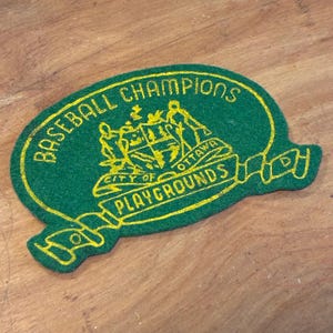 May include: A green felt patch with yellow text and graphics. The patch reads "BASEBALL CHAMPIONS" around the top edge and "CITY OF OTTAWA PLAYGROUNDS" at the bottom. The center features a shield and figures.
