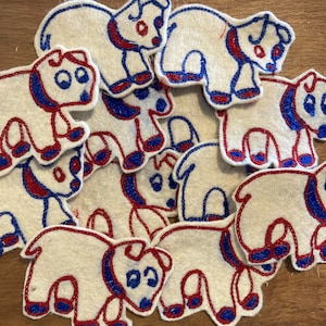 May include: A group of white felt polar bear appliques with red and blue embroidered details. The polar bears have blue eyes and red accents on their ears, feet, and noses. The appliques are arranged on a wooden surface.