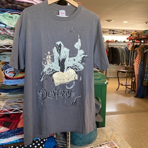 May include: A grey t-shirt featuring a graphic of a hooded figure holding a book with the text "Remember Now" and the word "Destiny" underneath.