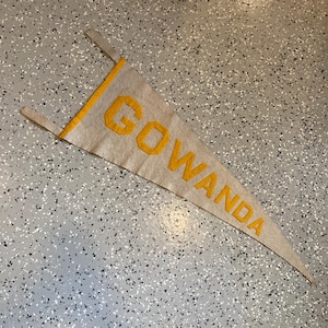 May include: A vintage felt pennant with the words "Go Wanda" in yellow lettering on a beige background.