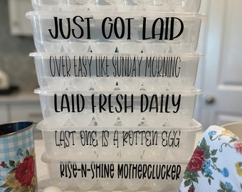 May include: A stack of six clear plastic egg storage containers with black text. The containers feature phrases including OVER EASY... JUST LIKE YOUR MOM, JUST GOT LAID, OVER EASY LIKE SUNDAY MORNING, LAID FRESH DAILY, LAST ONE IS A ROTTEN EGG, and RISE-N-SHINE MOTHERCLUCKER.