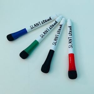 May include: Four white dry-erase markers with black caps and black lettering that says "SLANT stand". The markers are blue, green, black, and red.