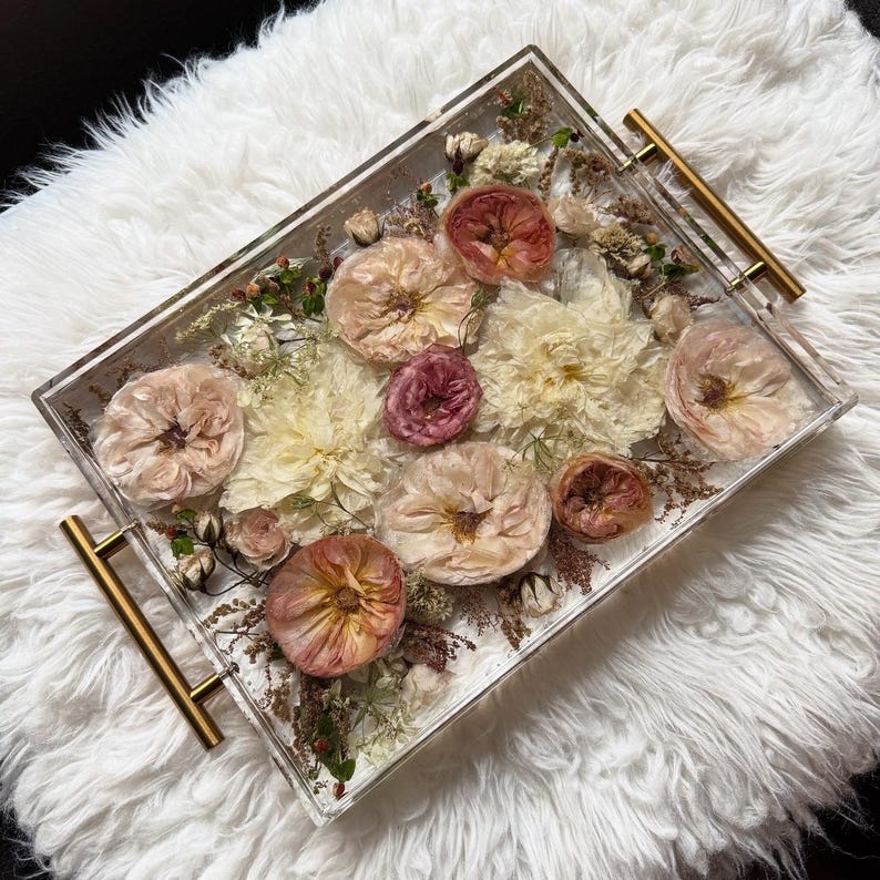 Op de afbeelding: Een transparant rechthoekig dienblad met gouden handvatten gevuld met geperste bloemen en groen. De bloemen zijn in tinten roze, wit en cr&egrave;me.