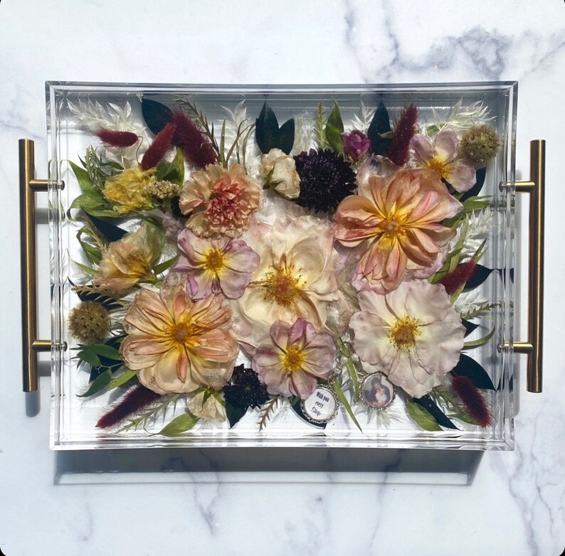 Op de afbeelding: Een transparante acryl dienblad met een geperst bloemenarrangement. De bloemen zijn in tinten roze, wit en bruin. Het dienblad heeft gouden handvatten en een kleine hanger met de tekst "You are my everything" is zichtbaar in het midden.