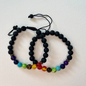 May include: Two black lava stone bracelets with adjustable cords. Each bracelet features seven colorful gemstone beads representing the seven chakras.