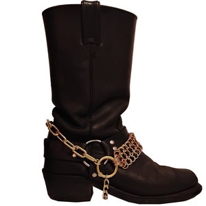 Peut inclure: Bottes de moto en cuir noir avec un détail de chaîne dorée autour de la cheville.