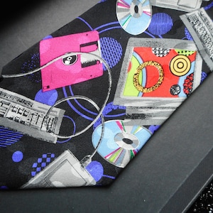 May include: A black silk tie with a colorful pattern of computer-related imagery, including floppy disks, CDs, and computer keyboards. The tie has a blue, purple, pink, red, green, and yellow color scheme.