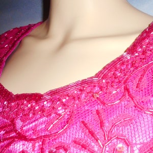 May include: A pink sequined top with a scoop neckline. The sequins are arranged in a floral pattern.