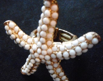 May include: A gold-tone adjustable ring featuring a white starfish design. The starfish is covered in small white beads.