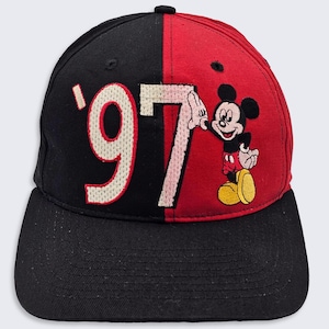Könnte beinhalten: Schwarze und rote Baseballkappe mit einer weißen '97' auf der schwarzen Seite und einem Mickey Mouse-Charakter auf der roten Seite.