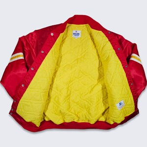 May include: Red satin baseball jacket with yellow lining and white and gold striped sleeves. The jacket has a snap closure and multiple buttons. The label on the inside reads "Pro Line Sportswear".