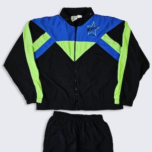 Puede incluir: Un chándal vintage negro, azul y verde neón. La chaqueta tiene cremallera, una sección superior azul y rayas verde neón. El texto "Magic" está impreso en el pecho izquierdo. Los pantalones cortos a juego son negros.