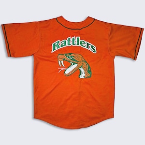 Könnte beinhalten: Orangefarbenes Baseballtrikot mit einem grünen und weißen Schlangenlogo und dem Wort "Rattlers" darüber.