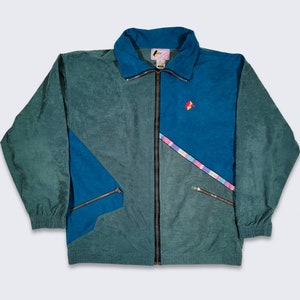 May include: A teal blue and dark green jacket with a zipper closure. The jacket has a geometric design with a blue panel and a pink and purple stripe. The jacket has a small red and yellow logo on the right side of the chest.