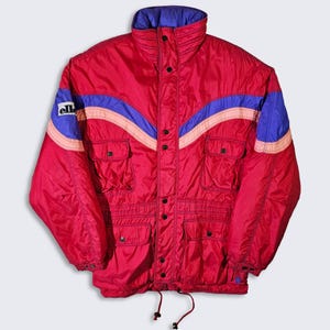 May include: A red ski jacket with blue and pink stripes and the word "elle" on the left sleeve. The jacket has a zipper closure and multiple pockets.