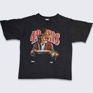 May include: Black t-shirt with a graphic of a man holding a pan with the text "San Francisco 49ers" in red.