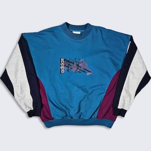Peut inclure: Un sweat-shirt Adidas vintage de couleur teal, avec des manches à blocs de couleurs grises, marine et blanches. Le devant présente un graphisme de coureurs et le logo Adidas. Le sweat-shirt a un col rond et des bords côtelés.