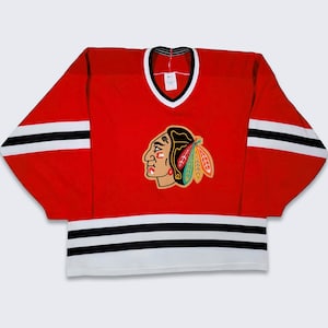May include: Red hockey jersey with black and white stripes and a black and white logo of a Native American head with a feather headdress.