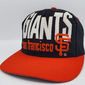 May include: A black and orange baseball cap with the word "Giants" and "San Francisco" embroidered on the front. The cap has an orange brim and a black crown.