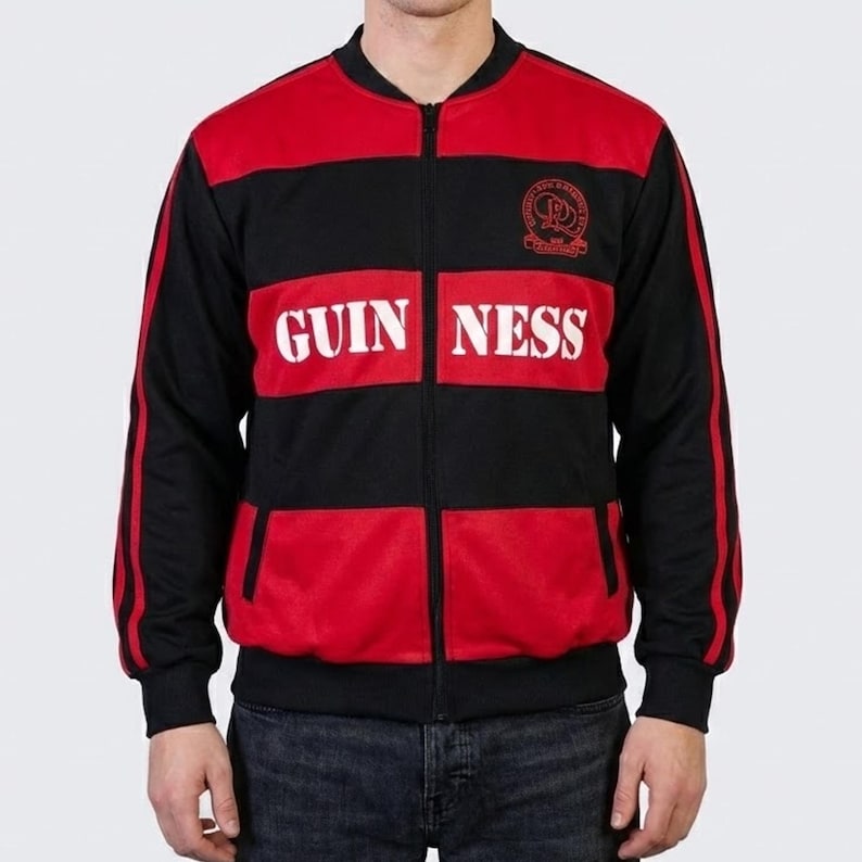 K&ouml;nnte beinhalten: Schwarz-rote Jacke mit Rei&szlig;verschluss und dem Wort "GUINNESS" in wei&szlig;en Blockbuchstaben auf der Brust. Die Jacke hat einen schwarzen Kragen, &Auml;rmel und R&uuml;cken mit roten Eins&auml;tzen auf der Vorderseite. Ein kleines Emblem ist sichtbar.