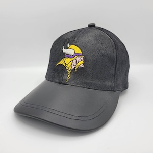 Puede incluir: Gorra de béisbol negra con visera de cuero negro y un logotipo bordado de los Minnesota Vikings en amarillo y morado.
