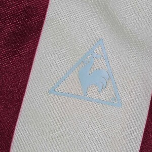 Puede incluir: Una camisa a rayas blancas y burdeos con un logotipo de gallo azul en un tri&aacute;ngulo en la parte delantera.