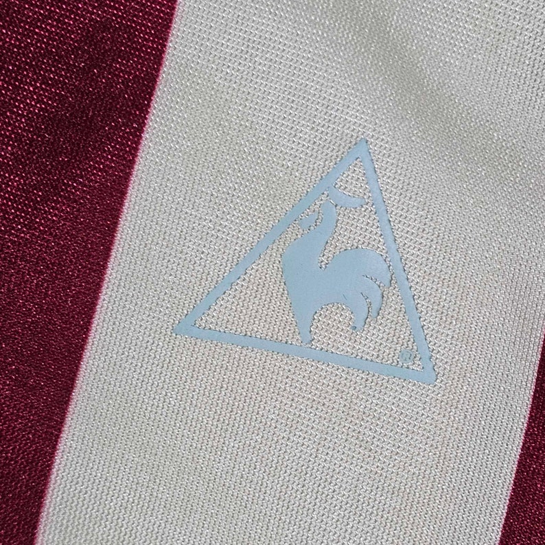 Puede incluir: Una camisa a rayas blancas y burdeos con un logotipo de gallo azul en un tri&aacute;ngulo en la parte delantera.