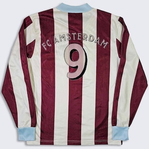 Puede incluir: Una camiseta de f&uacute;tbol de manga larga a rayas blancas y marrones con el texto "FC AMSTERDAM" y el n&uacute;mero "9" en la espalda.