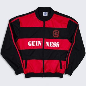 K&ouml;nnte beinhalten: Schwarz-rote Trainingsjacke mit Rei&szlig;verschluss und dem Wort "GUINNESS" in wei&szlig;en Blockbuchstaben auf der Vorderseite. Die Jacke hat einen roten Streifen an den &Auml;rmeln und ein Logo auf der oberen Brust. Gr&ouml;&szlig;e M.