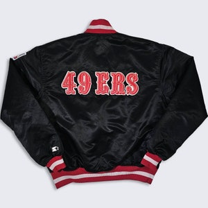 May include: Black satin bomber jacket with red and white striped cuffs and collar. The back of the jacket features a large red embroidered "49ERS" logo.