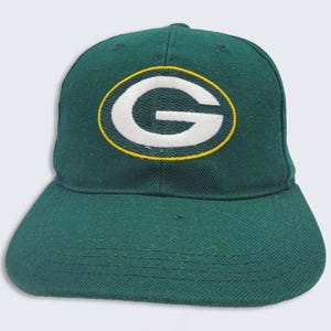 May include: Green baseball cap with a white "G" embroidered in a yellow circle on the front.